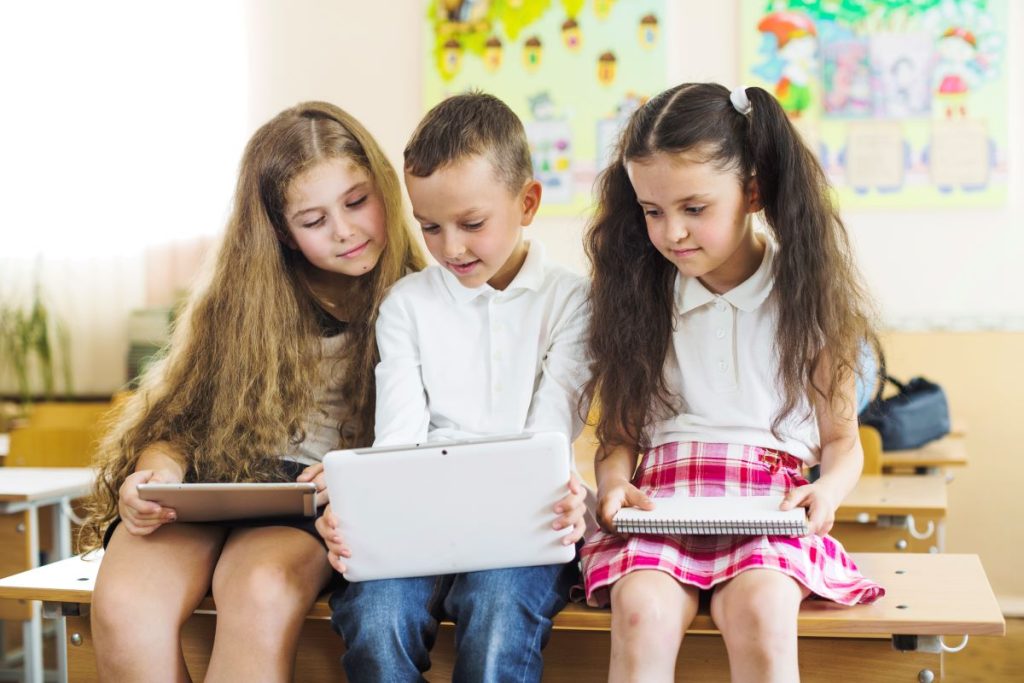 A group of learners sitting on the desk while looking at the laptop inside the classroom.